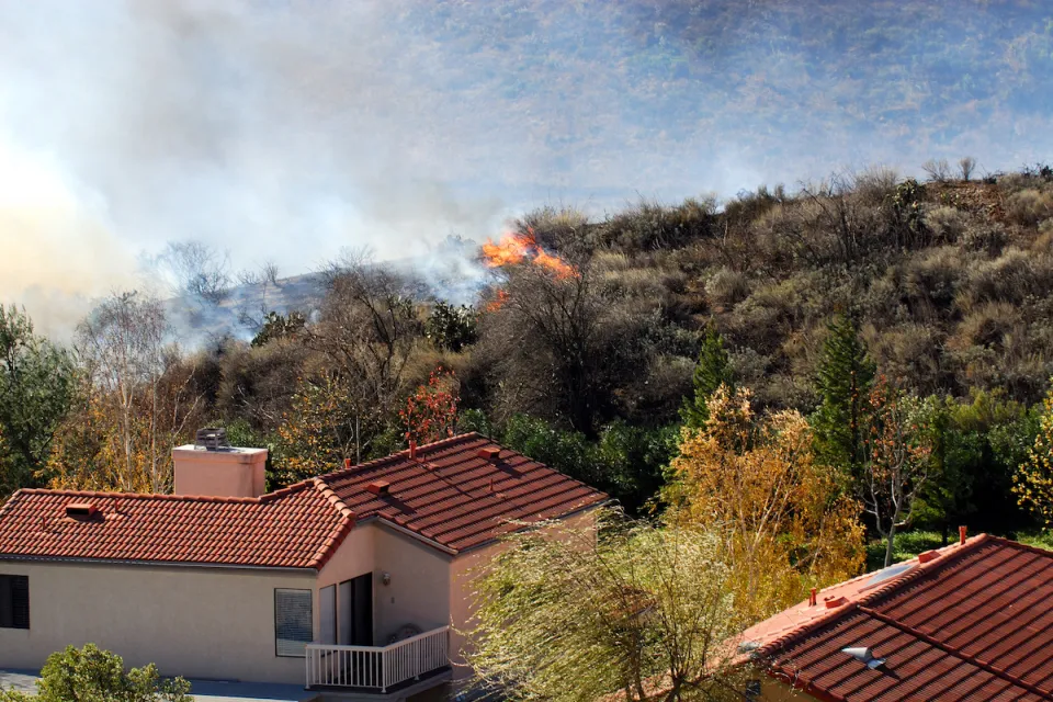 Wildfire approaching stucco house with red tile roof.